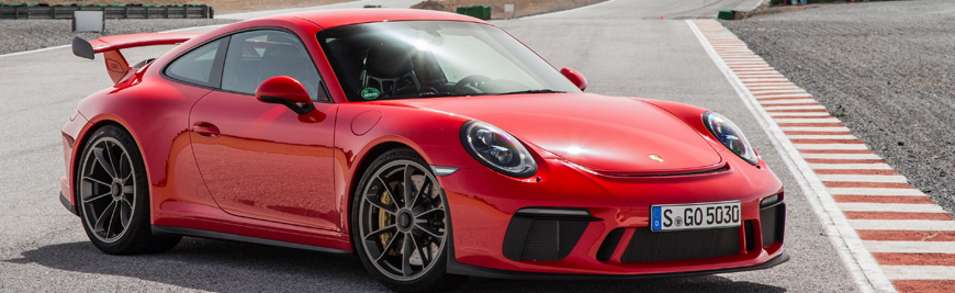 A red sports car on a race track with a rear spoiler, seen from a front-side angle.