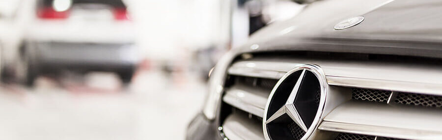 Why European Cars Need European Auto Repair Specialists. Closeup image of a Mercedes-Benz car grill at an auto repair shop, with another car in the background.