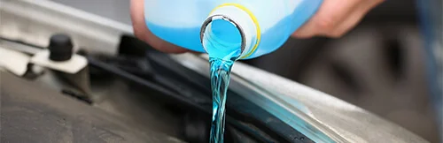 Fall Car Care Tips for European Cars | Heights Swedish Solutions in Cleveland Heights, OH. Closeup image of a man’s hand pouring blue antifreeze or coolant from a canister into a car engine.
