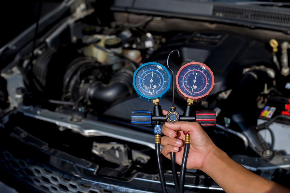 Auto A/C repairs and new auto air conditioning refrigerant in Cleveland Heights, OH with Heights Swedish Solutions. Image of mechanic hand holding up A/C Repair machine in front of car engine from a car that came in the shop for ac issues.